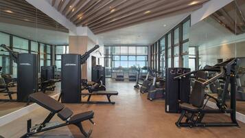 A gym with various exercise equipment, large windows, and a wooden ceiling.