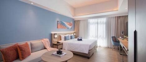 Une chambre d’hôtel moderne équipée d’un canapé, d’un lit, d’un bureau et d’une grande fenêtre.