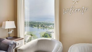Una habitación con vistas a un lago y edificios, un letrero que dice 'welcome', una lámpara y dos sillas.