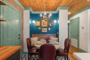 A dining area with a wooden ceiling, a round table with chairs, and wall-mounted lights. - Luxury Creole Cottage - Sleeps 6 guests (Lafayette)