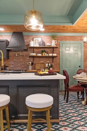 A kitchen with a central island, stools, a hanging light fixture, and a patterned floor.