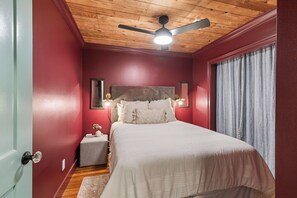 A bedroom with a wooden ceiling, a bed with white bedding, a nightstand, and a window with curtains.