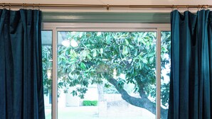 Un saló amb un sofà de cuir marró, una taula de centre de vidre i vista a un arbre a través d'una finestra amb cortines fosques.