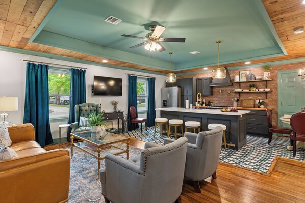 A modern kitchen with a central island, bar stools, a dining area with a sofa and chairs, and a ceiling fan. - Luxury Creole Cottage - Sleeps 6 guests (Lafayette)