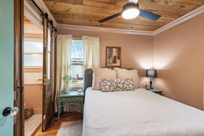 A bedroom with a bed, a nightstand, a lamp, a painting, and a ceiling fan.