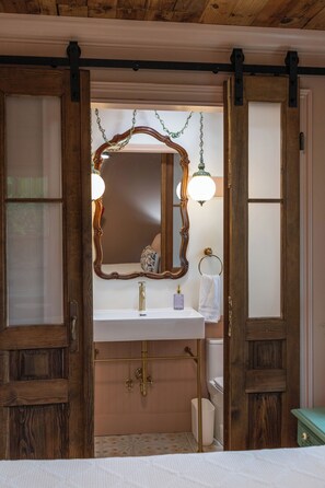 A bathroom with a wooden door, a white sink, a mirror with a decorative frame, and a towel rack.