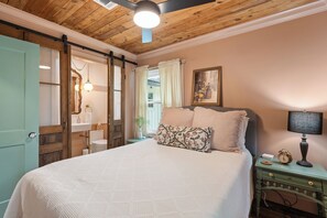 A bedroom with a bed, a nightstand with a lamp, a painting on the wall, and a wooden ceiling. - Luxury Creole Cottage - Sleeps 6 guests (Lafayette)