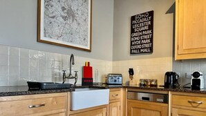 A modern kitchen with wooden cabinets, a black countertop, and a wall-mounted sign listing nearby locations. - Chester Centre 2-bed Apartment -by Oddfellows (Chester)