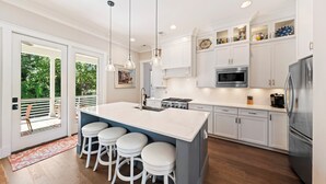 A modern kitchen with white cabinets, a large island with bar stools, stainless steel appliances, and a view to the outdoors.