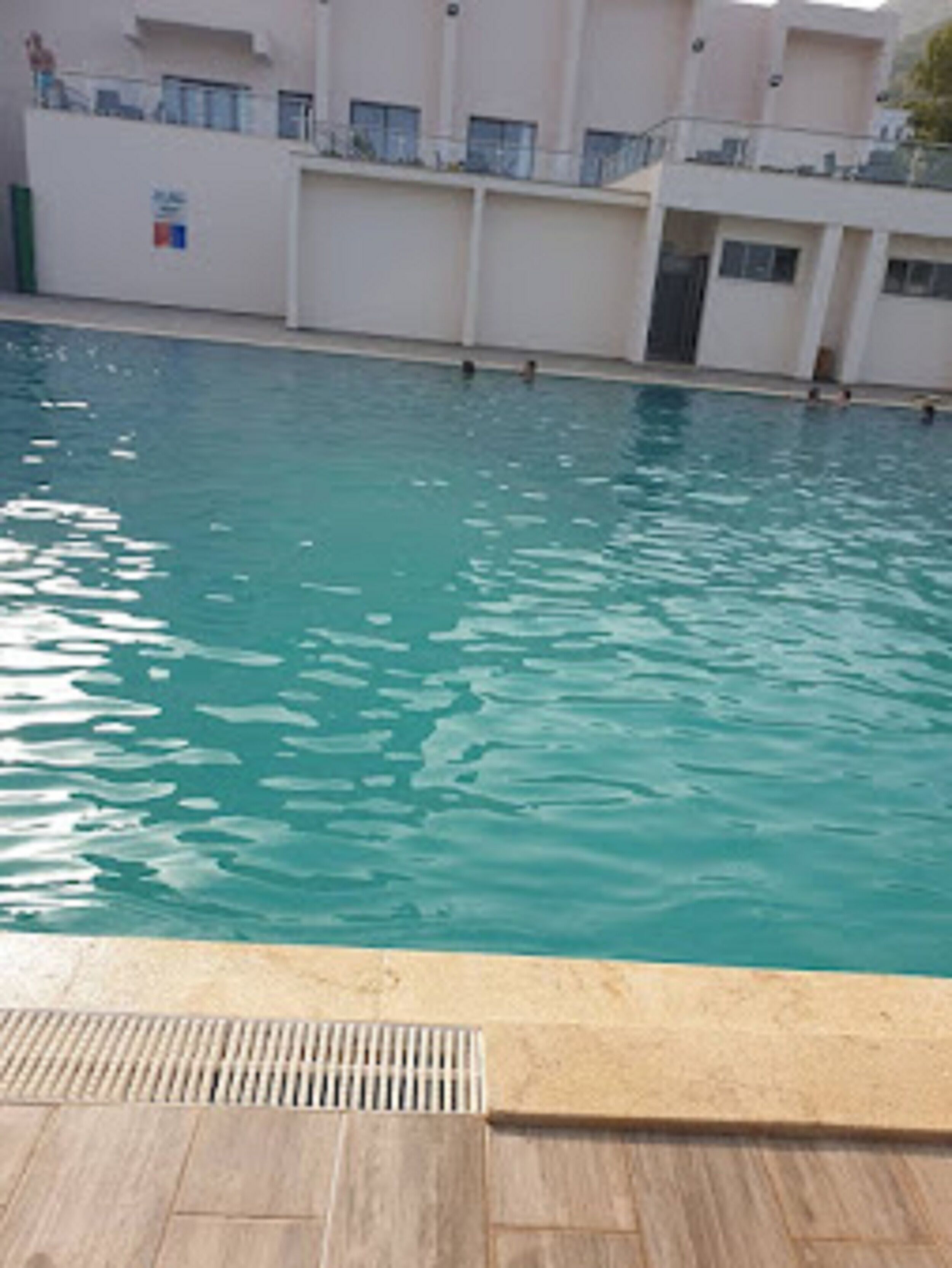 En swimmingpool med klart vand, omgivet af en bygning med altaner.
