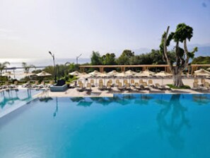 A large swimming pool with lounge chairs and umbrellas, surrounded by trees and a view of the ocean. - SALDAE HOTEL BEJAIA (Béjaïa)