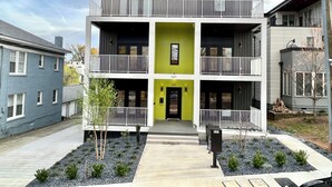 Een modern meerlaags gebouw met balkons, een groene accentmuur en een heldere lucht.