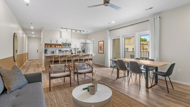 Een moderne woonkamer met een bank, een eettafel en stoelen, een keuken op de achtergrond, en een balkon met uitzicht.