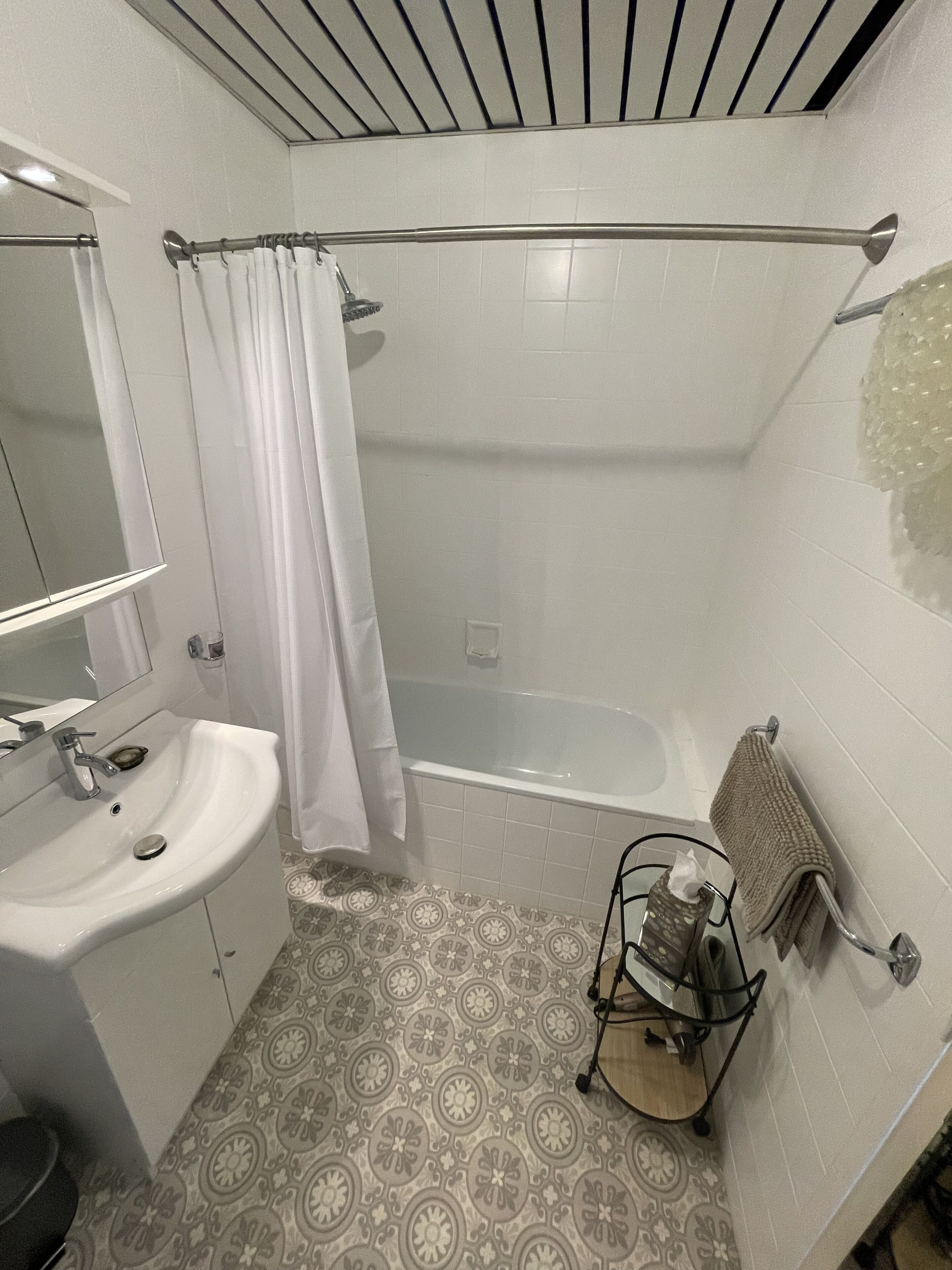 Un baño con bañera, lavamanos, espejo, toallero y baldosas de suelo estampadas.