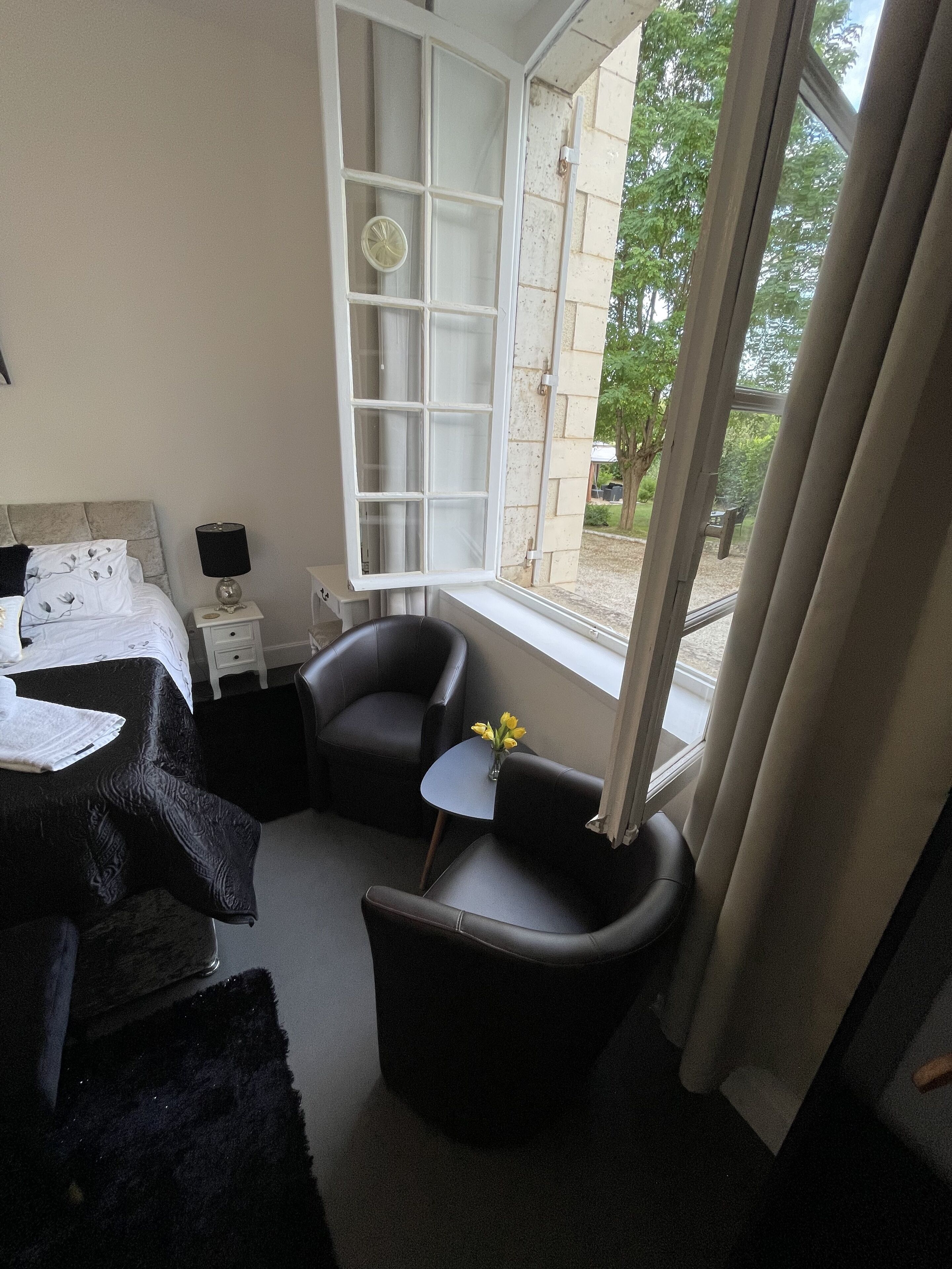 A hotel room with a bed, two armchairs, a small table with flowers, a window, and a view of the outside.