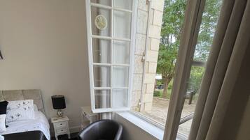 A hotel room with a bed, two armchairs, a small table with flowers, a window, and a view of the outside.