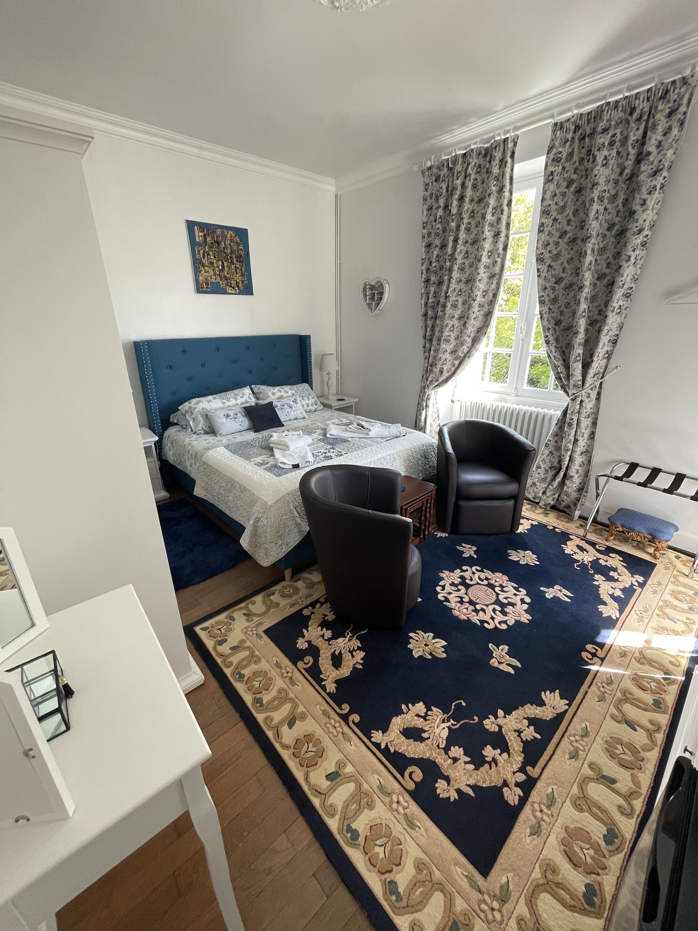 Een slaapkamer met een bed, een stoel, een klein tafeltje en een raam met gordijnen.