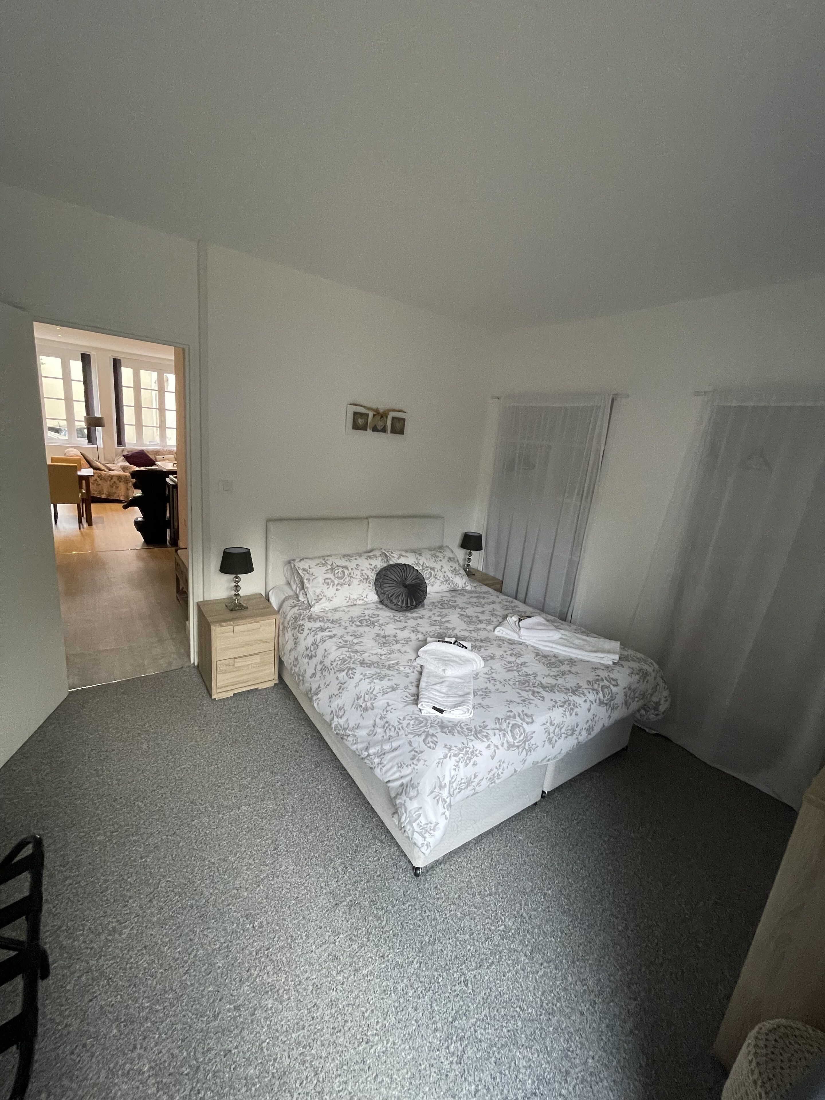 Une chambre avec un grand lit, une table de chevet, une lampe et une vue sur un espace de vie comprenant un canapé et un fauteuil.