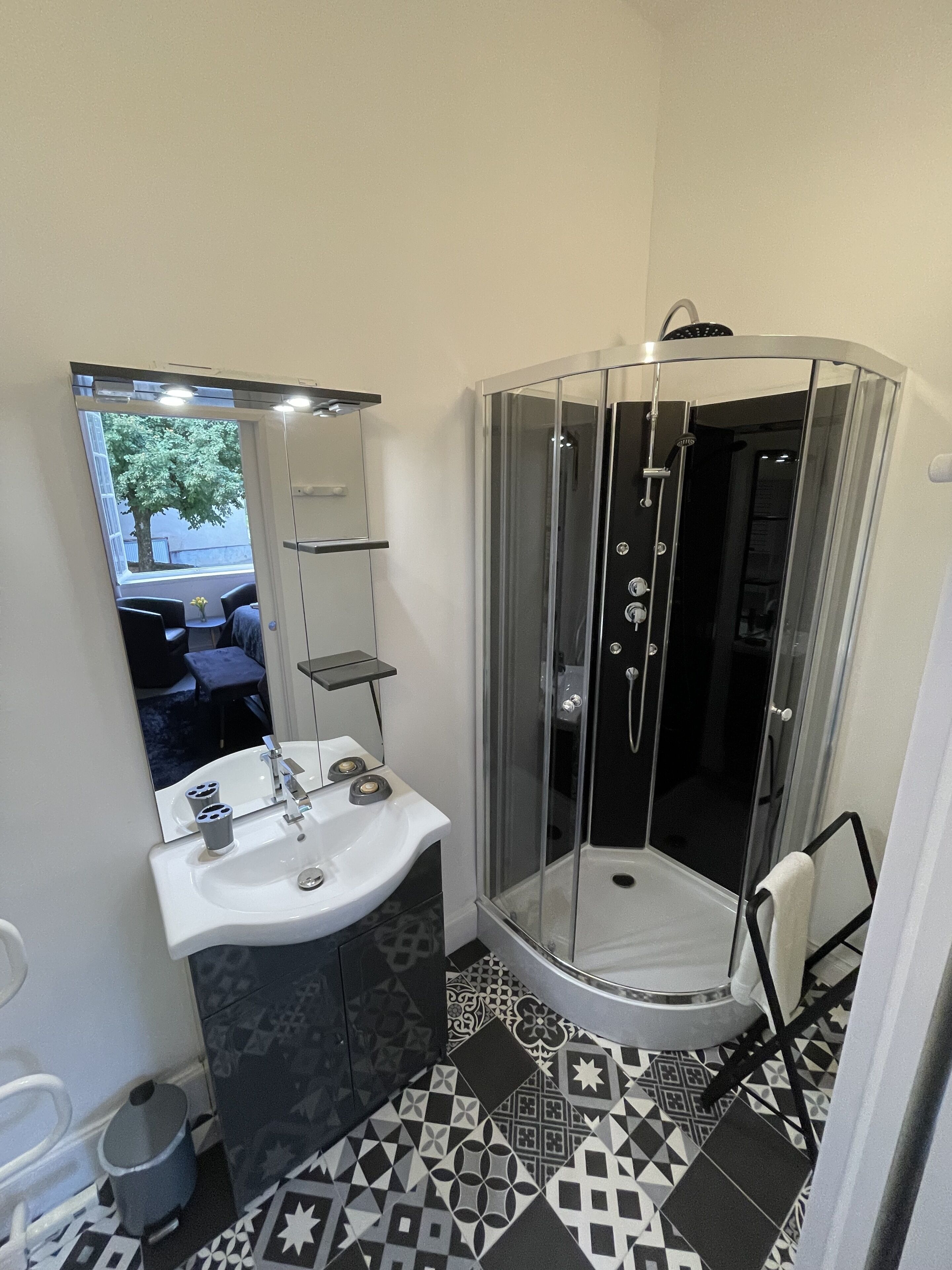 Un baño moderno con ducha envuelta en vidrio, un lavabo blanco con espejo y baldosas de suelo estampadas.