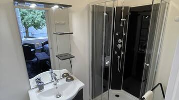 Un baño moderno con ducha envuelta en vidrio, un lavabo blanco con espejo y baldosas de suelo estampadas.