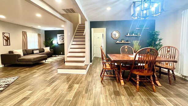 A spacious living room with a wooden floor, a dining area with a wooden table and chairs, a staircase, and a ceiling light fixture. - Super Spacious Safari Retreat.. Lots of SPACE-Deck + Grill,  near Memphis/Desoto (Southaven)