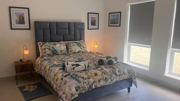 Un dormitorio con una cama grande, dos mesitas de noche con lámparas, un ventanal con vistas y cuadros enmarcados en la pared.