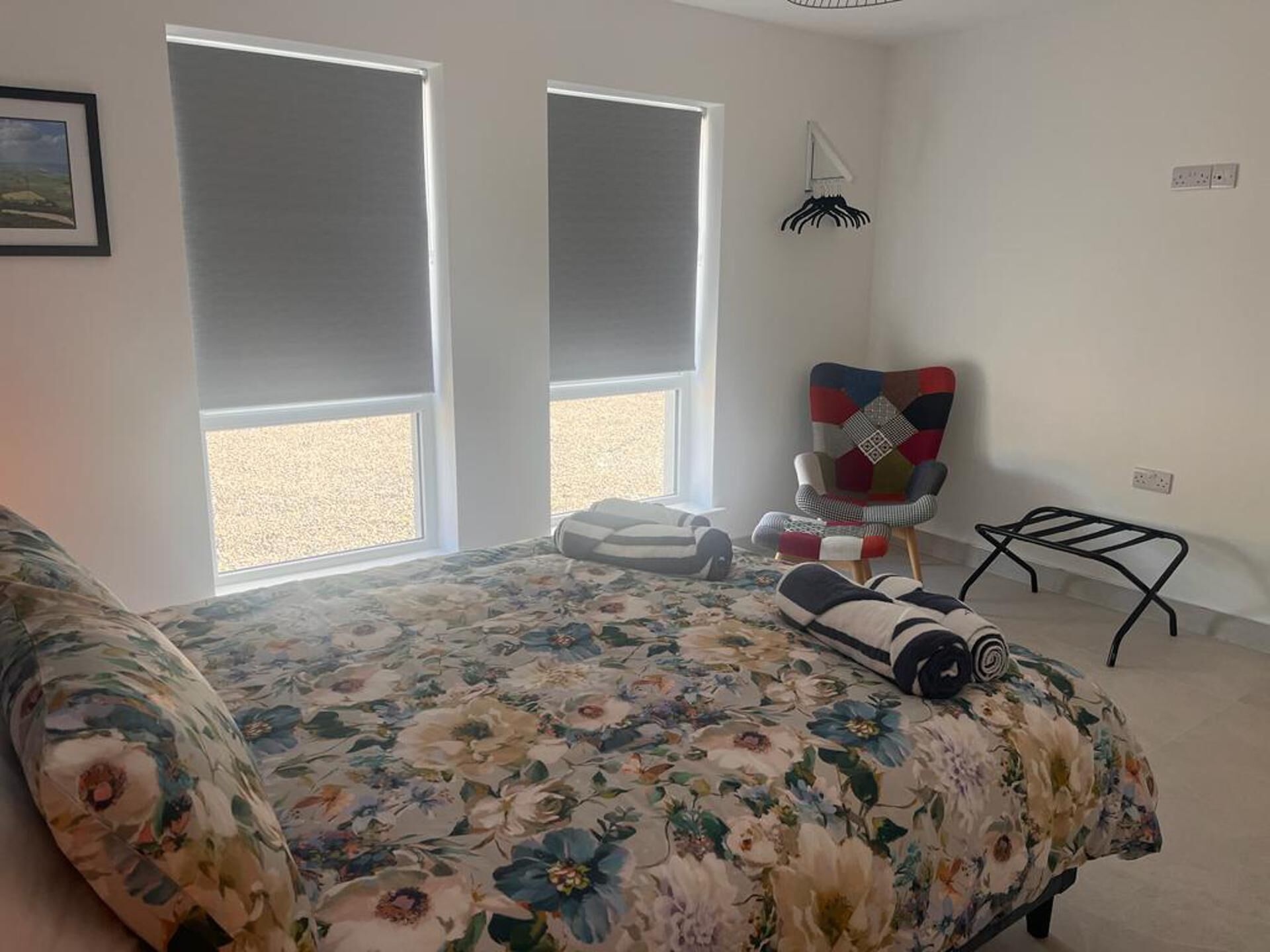 Een slaapkamer met een bloemenbedekker, een kleurrijke stoel en een klein tafeltje.