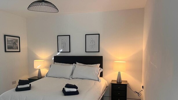 A neatly made bed with white linens, two bedside tables with lamps, and a large window with a view.