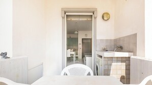 Una habitación pequeña y limpia con una mesa blanca, una silla, un lavamanos y una ventana.