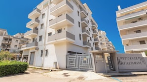 Un edificio residencial de varios pisos con entrada porticada, balcones y un cielo azul despejado.