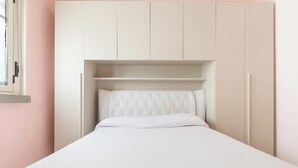 Una cama con cabecera, un estante encima y una ventana a la izquierda.