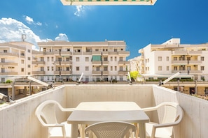Une terrasse avec une table et des chaises, donnant sur une rangée d’immeubles d’habitation.