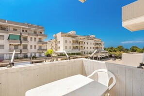 Un balcon avec une chaise blanche et une table, d’où l’on peut admirer une rangée d’immeubles dotés de balcons, ainsi qu’un ciel bleu dégagé.