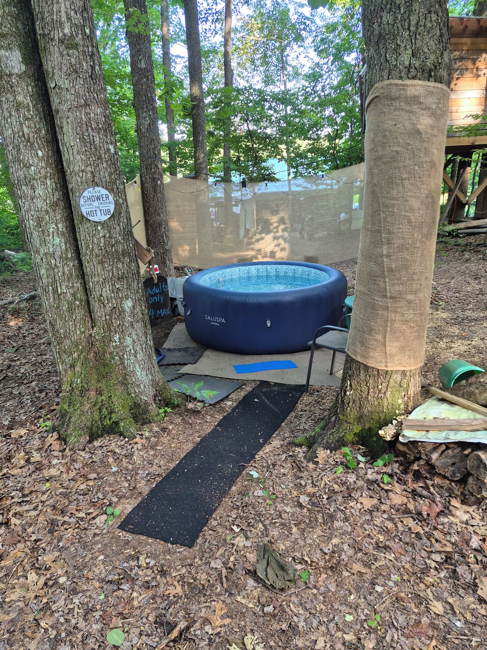 A hot tub surrounded by trees, a sign indicating it is for adults only, and a sign requesting shower before entering.