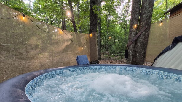 Un jacuzzi rodeado de árboles, con luces colgantes y una silla.