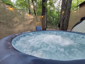 A hot tub surrounded by trees, with string lights and a chair. - Driftwood Treehouse Cabin w/AC, Peaceful & Cozy! (Grandview)