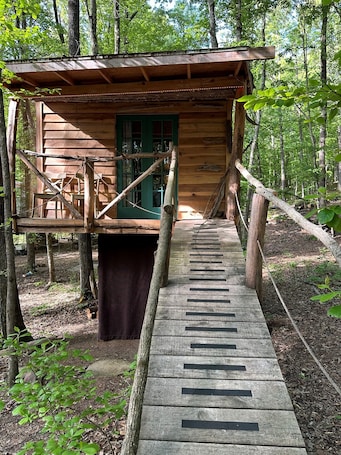 A wooden cabin with a wooden deck leading to a green door, surrounded by trees.. Driftwood Treehouse Cabin w/AC, Peaceful & Cozy!
