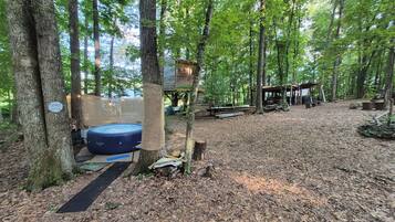 A forested area with a hot tub, a shower sign, and a wooden structure.