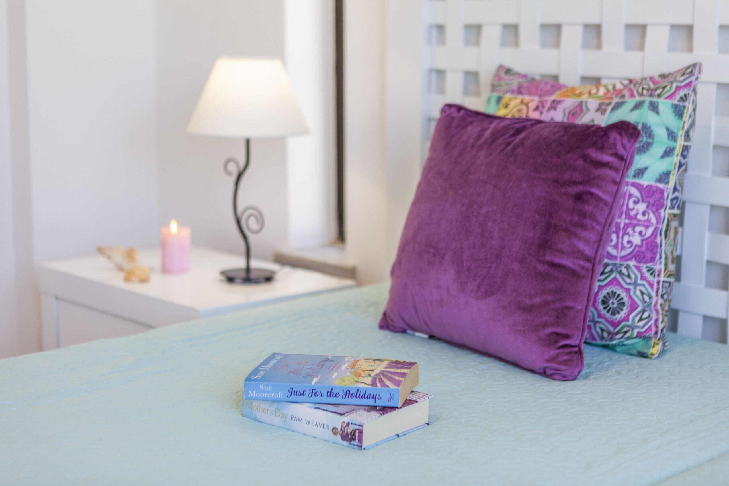A bed with a light blue bedspread, a purple pillow, and two books titled 'Just For the Holidays' and 'Mother's Day'.