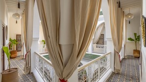 A corridor with beige curtains tied at the ends, potted plants, and a balcony with a white railing. - Riad Safran et Soleil (Marrakech)