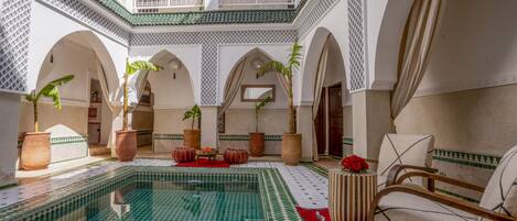 A traditional Moroccan interior with a central pool, arches, and tiled flooring.