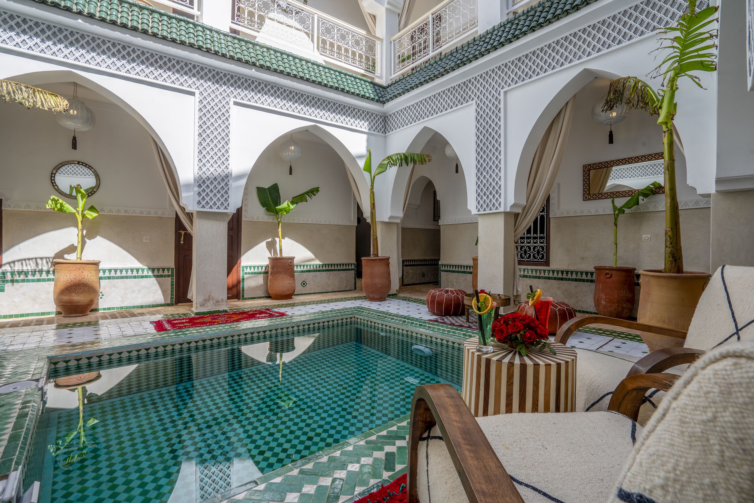 A traditional Moroccan interior with a tiled swimming pool, arches, and potted plants.