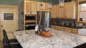 Eine Küche mit Holzschränken, einem Edelstahl-Kühlschrank, einer Granitarbeitsplatte und einem Essbereich mit schwarzen Ledersesseln.
