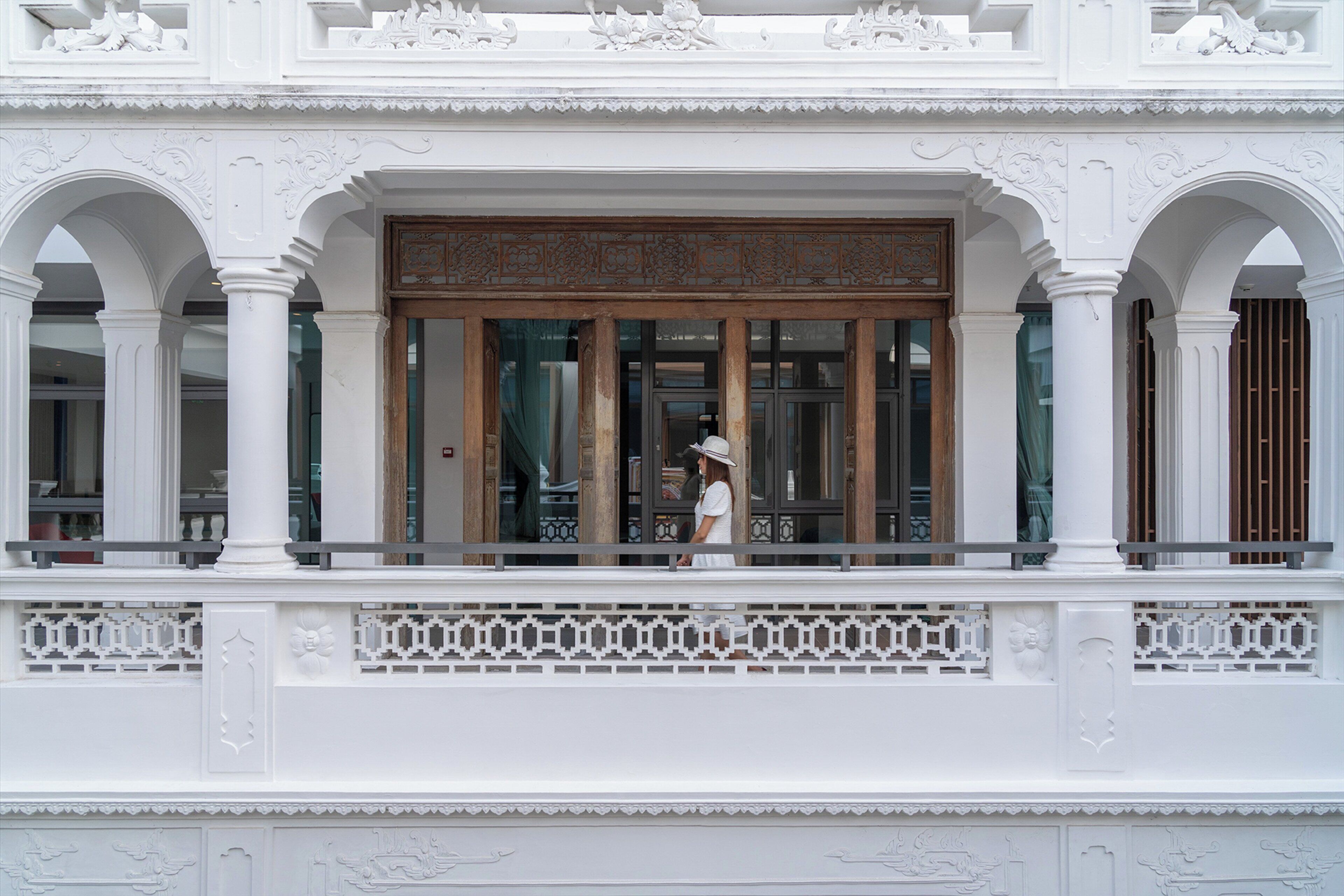 Fachada de edificio con detalles blancos ornamentales, ventanas grandes y un balcón con barandilla.