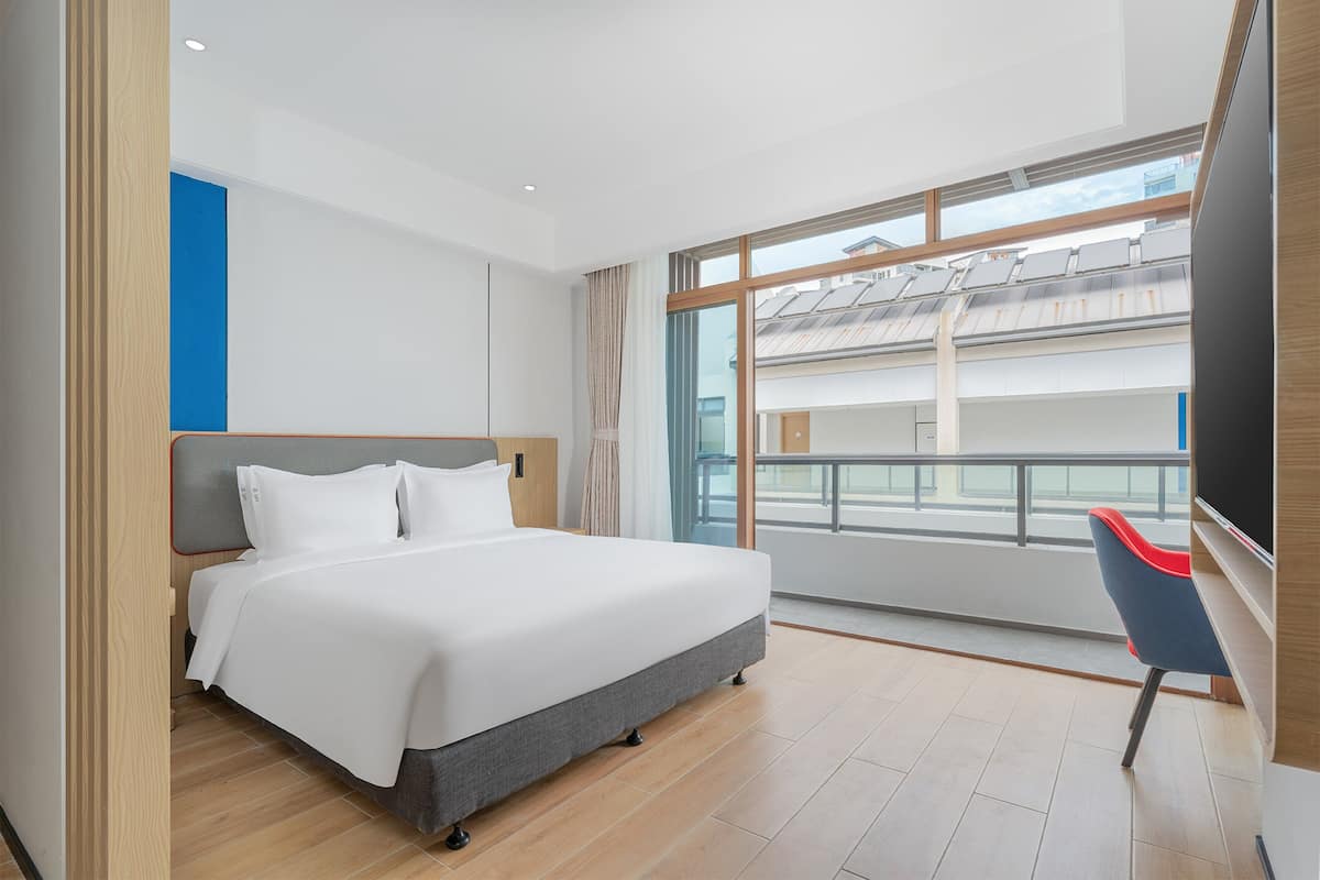 A modern hotel room with a large bed, a view of a balcony, and a chair.