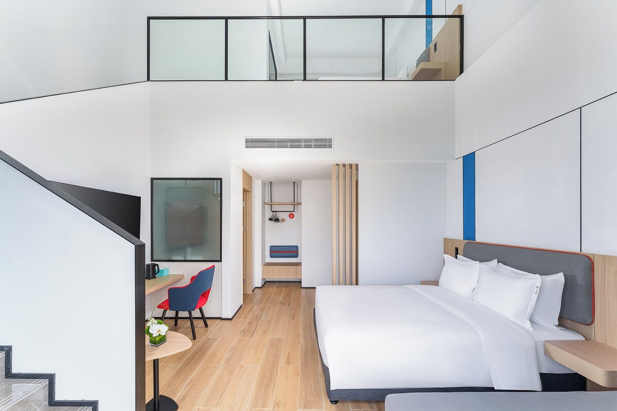 A modern hotel room with a large bed, a desk, and a seating area.