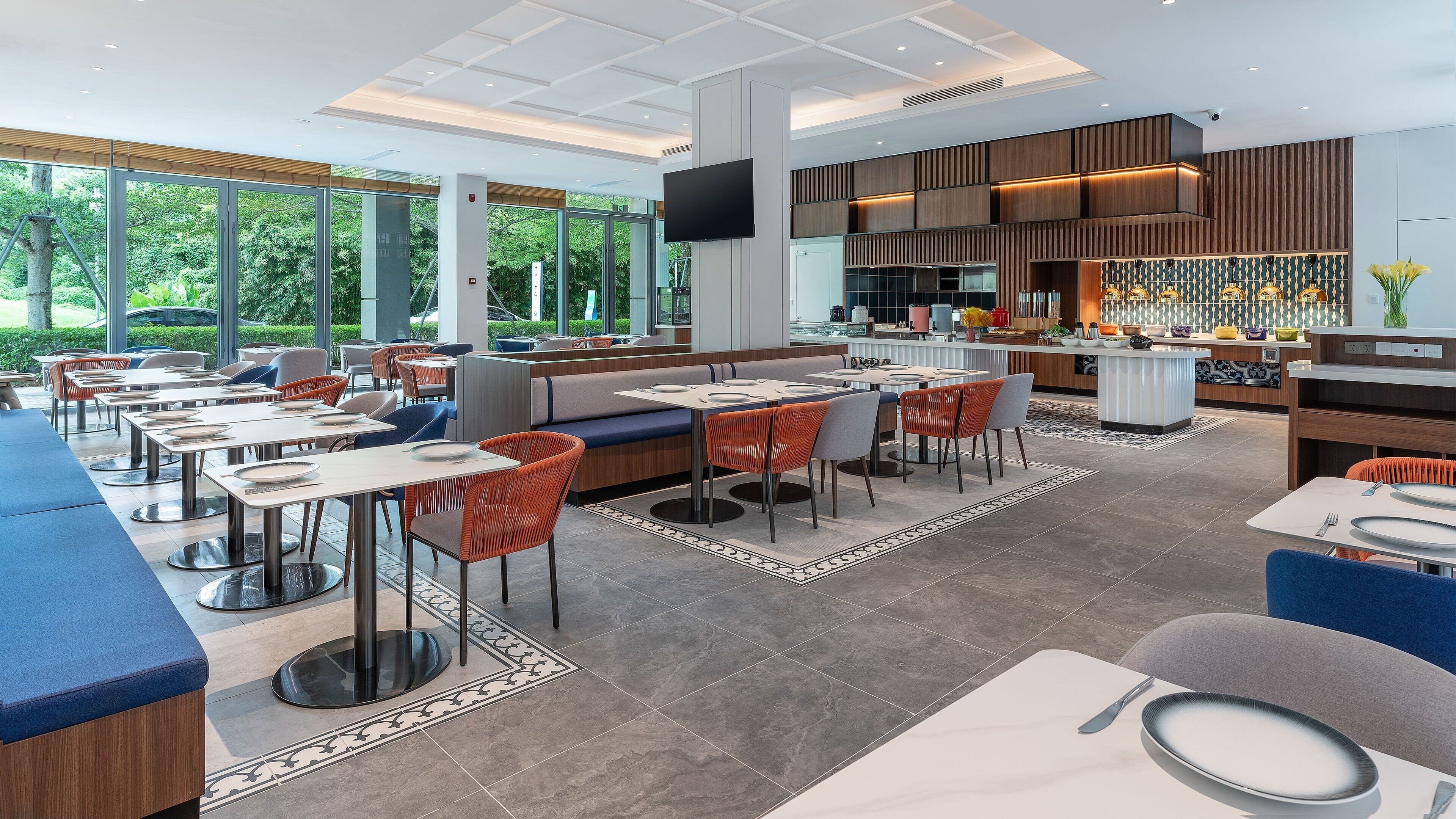 Un restaurant moderne doté de hauts plafonds, de grandes fenêtres et proposant différents types de sièges, notamment des banquettes et des tables.