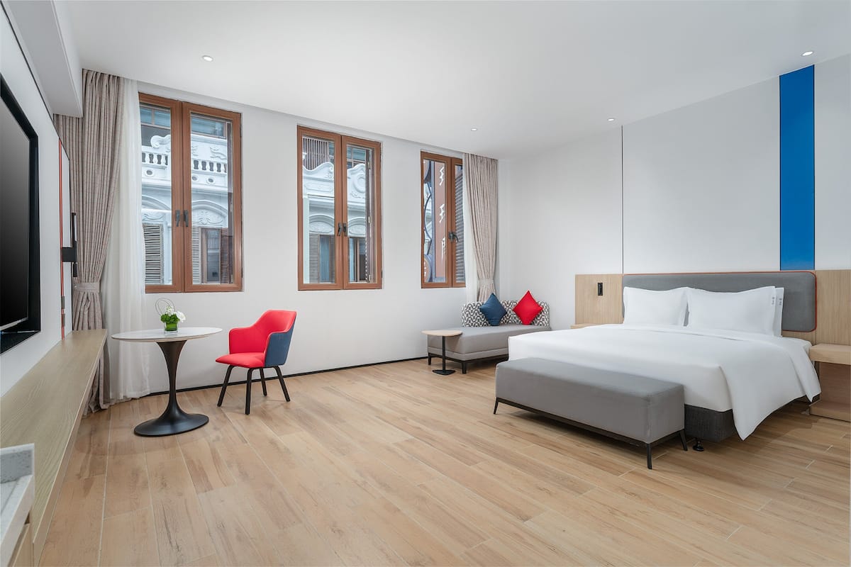 A modern hotel room with a bed, a small table, a red chair, and a sofa.
