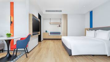 Una habitación de hotel moderna con una cama, un escritorio con silla, un televisor y una pequeña mesa con una planta.