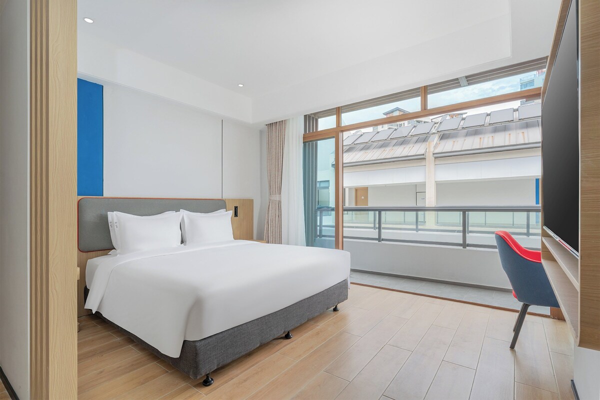 A hotel room with a large bed, a view of the city, and a balcony.